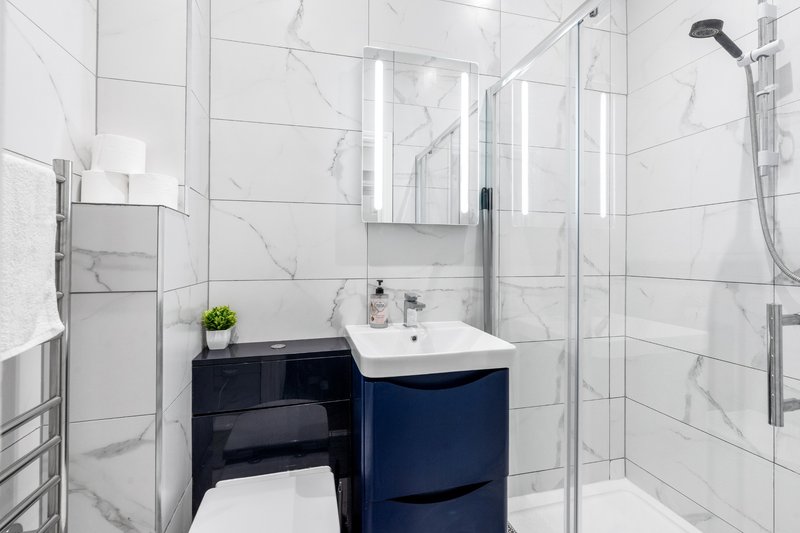 Modern bathroom with marble tiles, navy vanity, mirror, and walk-in shower enclosure