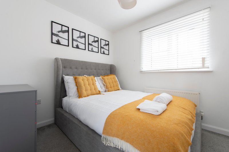 Bedroom with gray upholstered bed, yellow and white bedding, wall art, and window with blinds