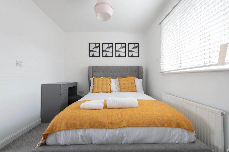 Bright bedroom with double bed, mustard duvet, decorative wall art and window blinds