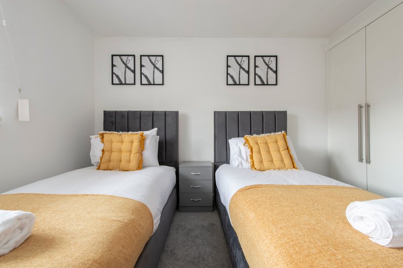 Twin bedroom with two single beds, yellow cushions, dark headboards and wall art