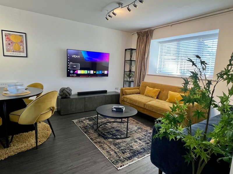 Modern living room with yellow sofa, gray armchair, wall-mounted TV, and potted plants