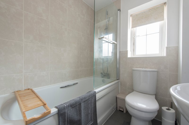 Modern bathroom with shower enclosure, toilet, sink and wooden bath rack