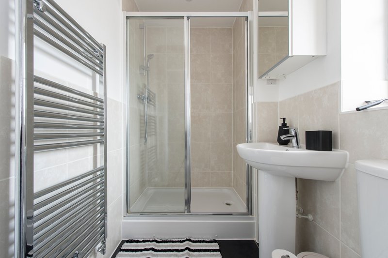 Modern bathroom with shower enclosure, pedestal sink, heated towel rail and white tile walls