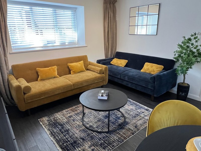 Bright living room with two sofas, round coffee table, plant, and window with blinds