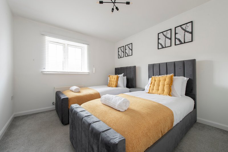 Modern bedroom with two double beds, yellow bedding, grey upholstered headboards and window