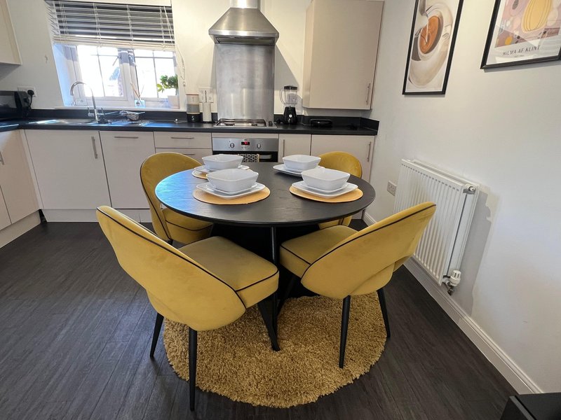 Modern kitchen-diner with round black table, yellow chairs, place settings and stainless steel hood