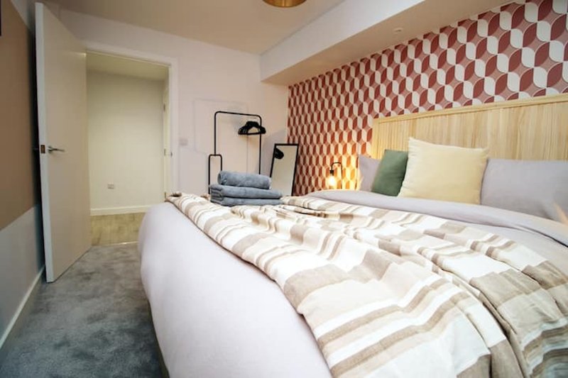 Modern bedroom with double bed, geometric wallpaper, bedside lamps and open door to bathroom
