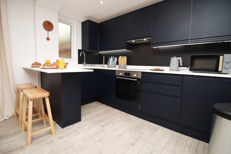 Modern kitchen with black cabinetry, white countertop, wooden stool, and breakfast bar