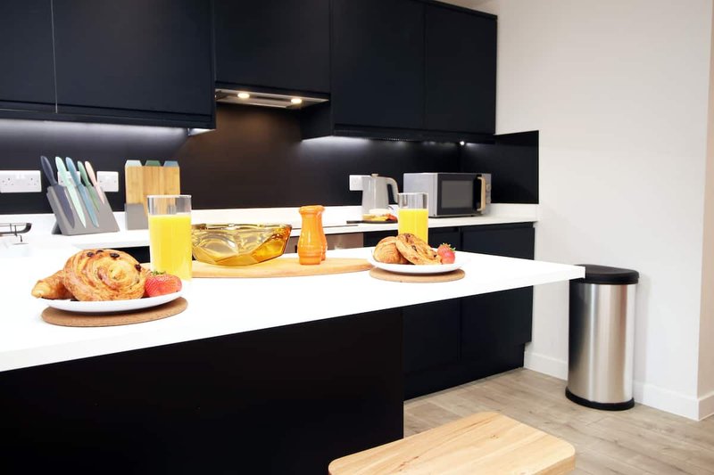 Modern kitchen with black cabinetry, white countertop, breakfast items and beverages displayed