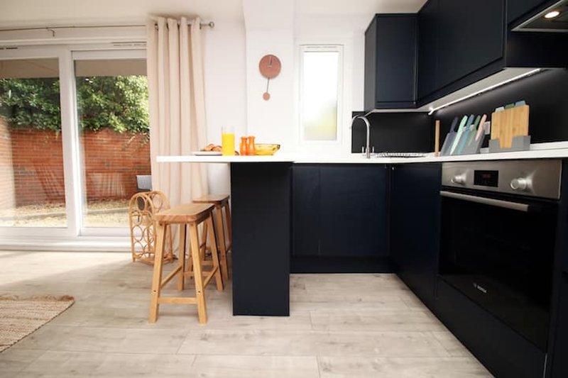 Modern kitchen with black cabinetry, white countertop, wooden bar stools and garden view