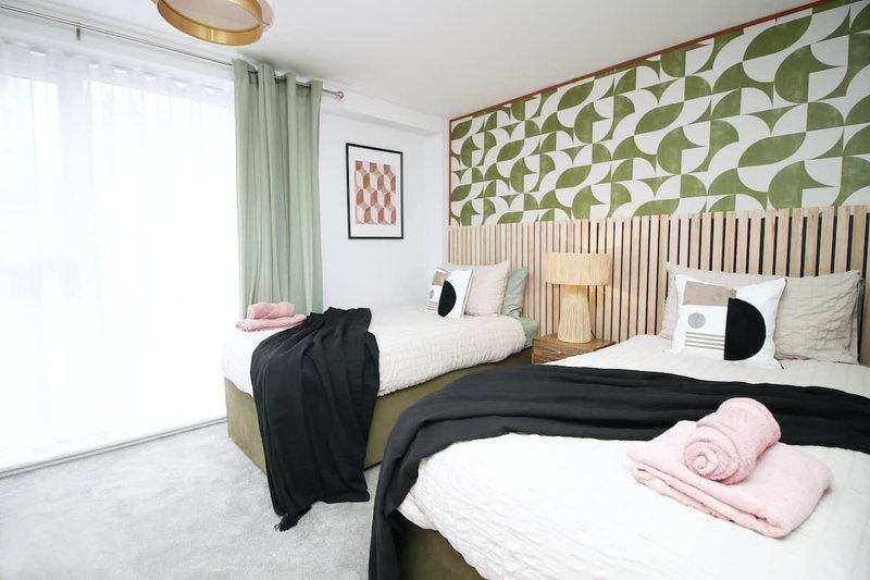 Modern twin bedroom with geometric green headboard, white bedding, and natural light from windows