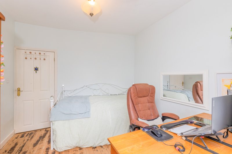 Bedroom with single bed, orange chair, desk, wooden floor and white walls