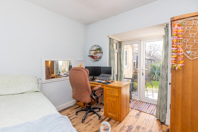 Bright bedroom with single bed, wooden desk, office chair and glass doors opening to garden