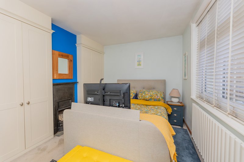 Bedroom with double bed, yellow bedding, fitted wardrobes, blue wall feature, and shuttered window
