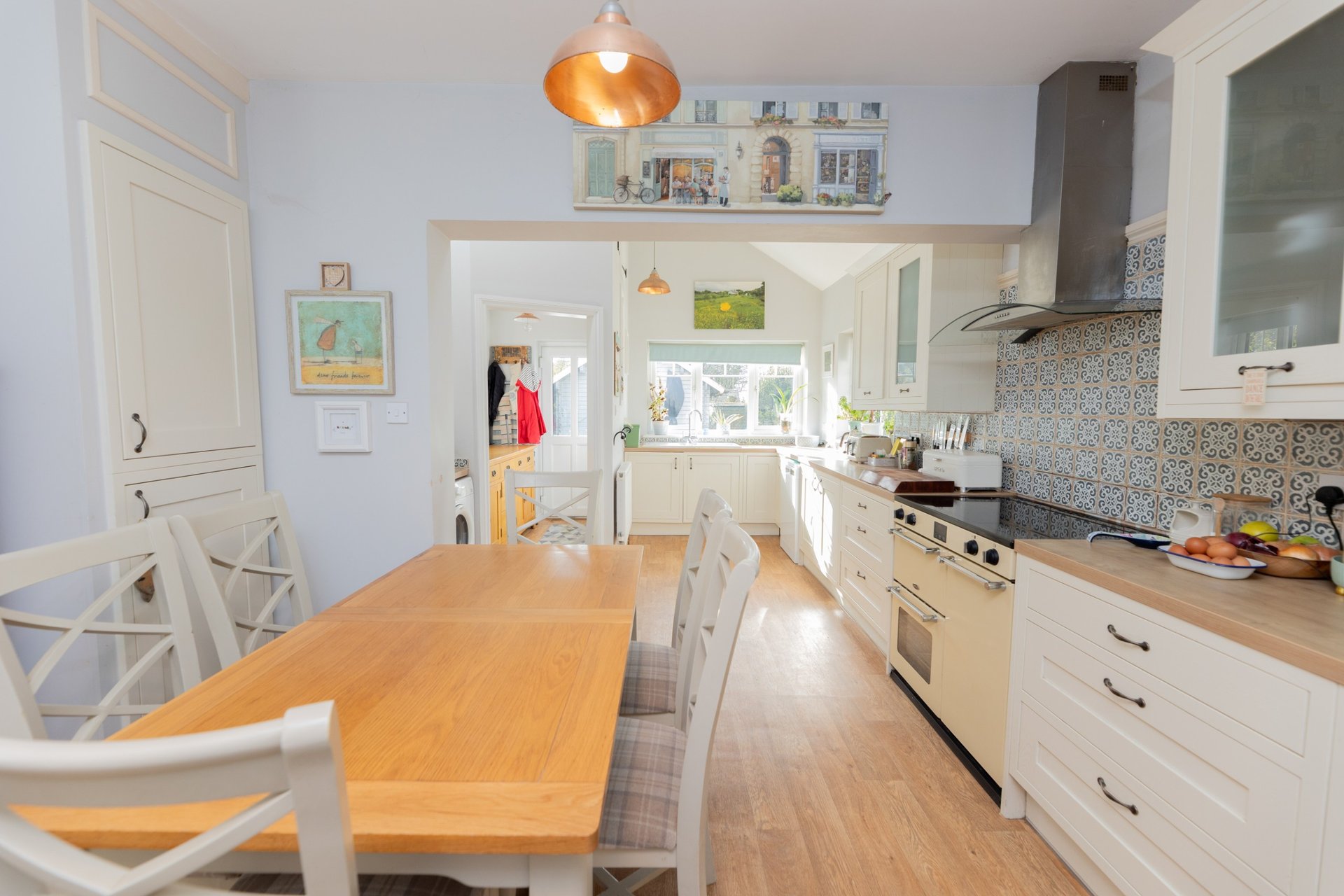 Bright modern kitchen with wooden dining table, cream cabinetry, orange pendant light and stainless steel appliances