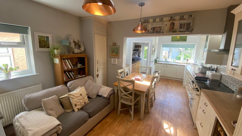 Open-plan living area with gray sofa, wooden dining table, kitchen with white cabinets, and copper pendant lights