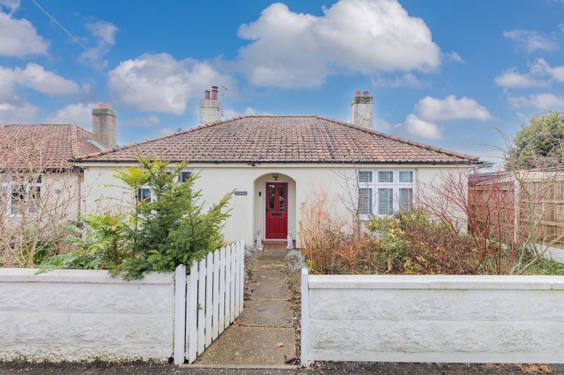 Single-storey bungalow with white render, red door, tiled roof and front garden