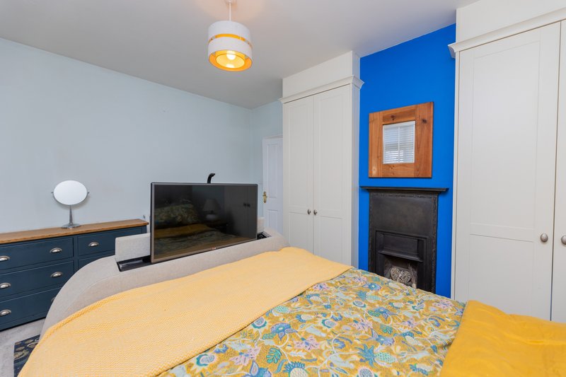 Bedroom with double bed, TV, blue accent wall, fireplace and white wardrobes
