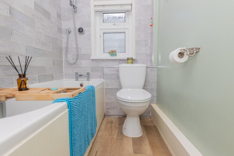 Modern bathroom with white subway tile, wooden vanity, toilet, shower, and blue towel