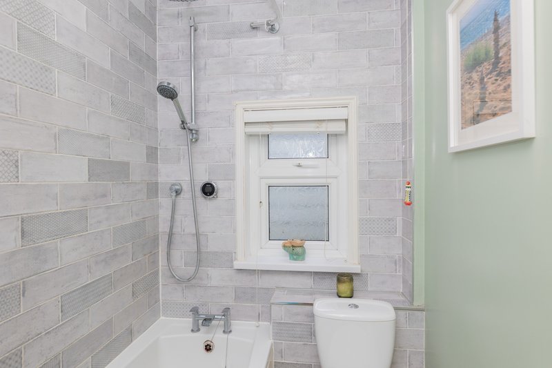 Modern bathroom with gray subway tile shower, white toilet, and window above sink