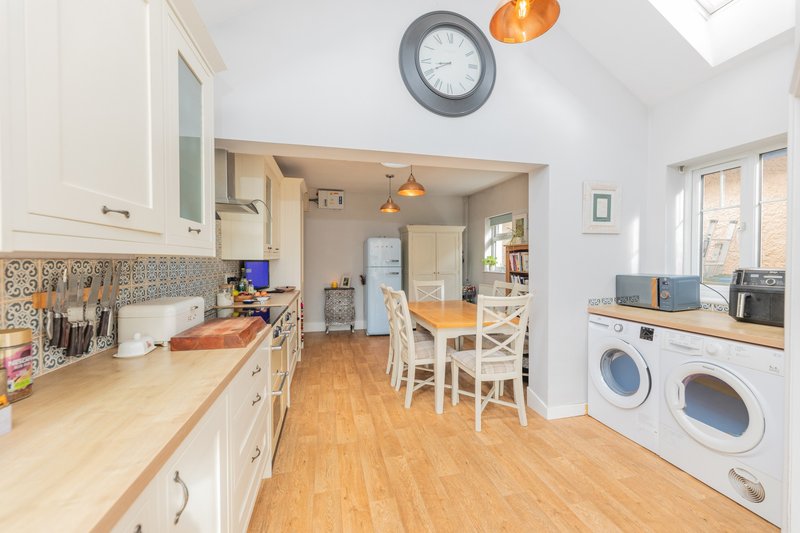 Open-plan kitchen and dining area with cream cabinets, wooden worktops, dining table, and white appliances