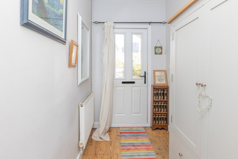 Bright hallway with white door, wooden floor, framed artwork and colorful runner rug