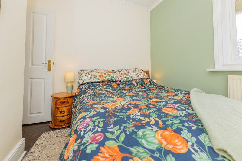 Bedroom with colorful floral bedding, wooden nightstand, table lamps and green accent wall