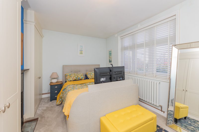 Bright bedroom with yellow bedding, dark furniture, shuttered windows and yellow ottoman