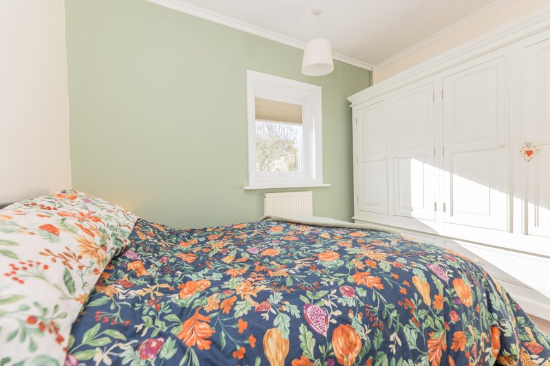 Bright bedroom with twin beds, floral bedding, green accent wall and white wardrobe