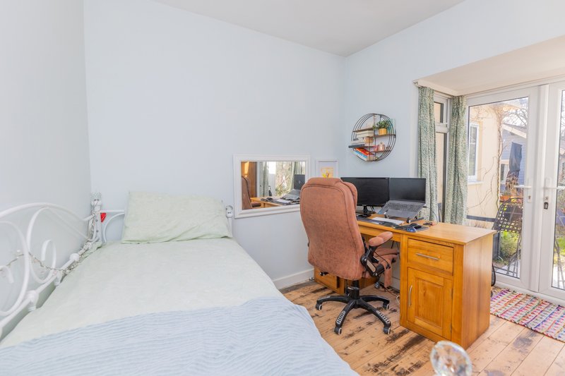 Bright bedroom with two single beds, wooden desk, office chair and glass door to garden