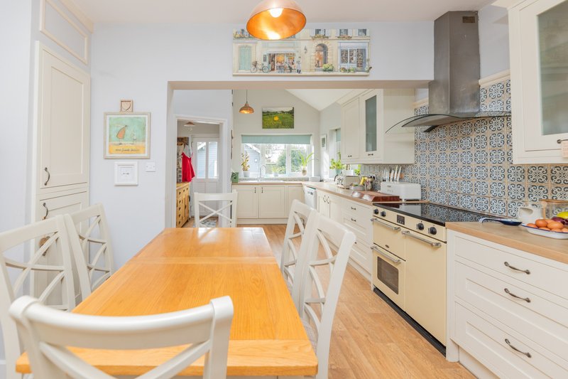 Bright kitchen with wooden dining table, white cabinetry, patterned backsplash and pendant lighting