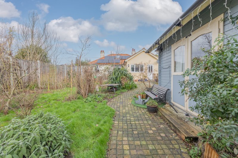 Garden patio area with paved pathway, lawn, potted plants and house exterior visible