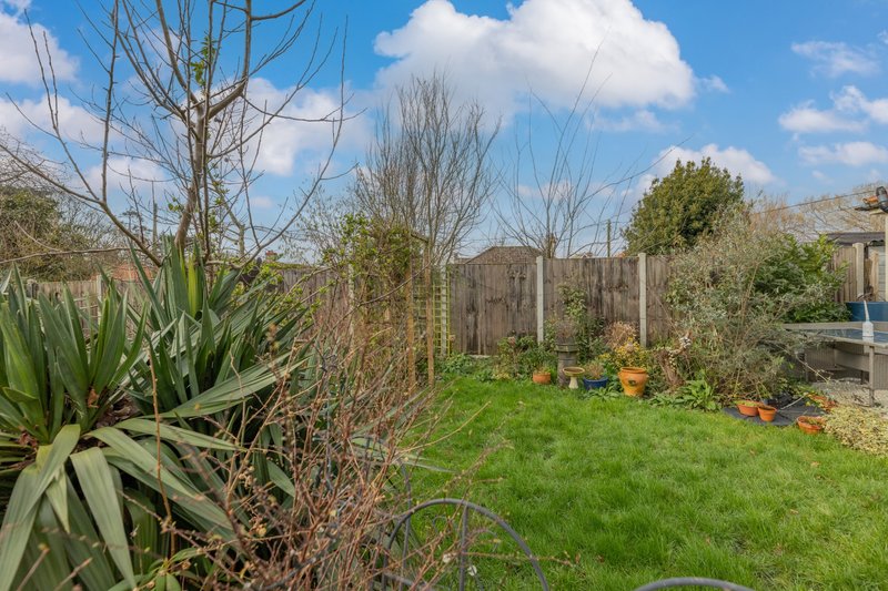 Garden area with green lawn, bare trees, shrubs, and wooden fence boundary