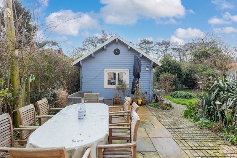 Blue garden studio with patio, outdoor dining table and seating area surrounded by plants