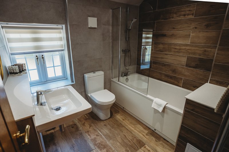 Modern bathroom with white sink, toilet, bathtub and wood-tiled shower enclosure