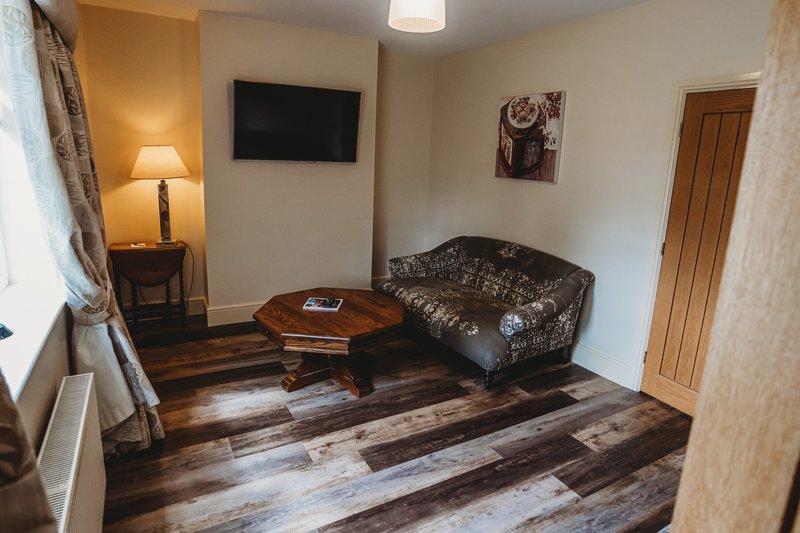 Living room with dark patterned sofa, wooden coffee table, wall-mounted TV, and lamp