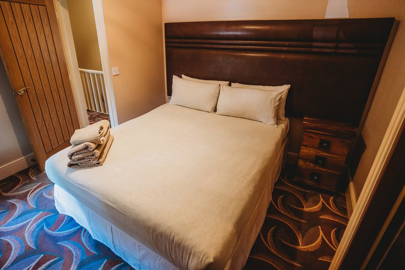 Bedroom with wooden bed frame, cream bedding, dark headboard, and patterned blue carpet floor.