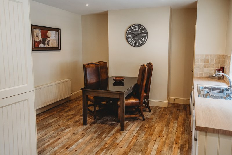 Dining area with wooden table, two chairs, wall clock, and framed artwork