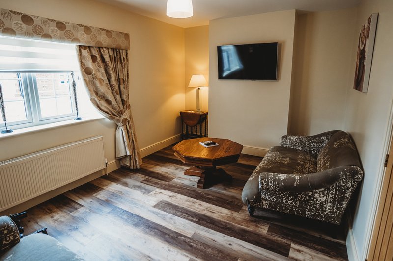 Living room with patterned armchair, wooden coffee table, wall-mounted TV and window with curtains