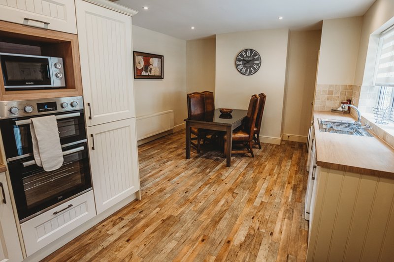 Open-plan kitchen and dining area with wood flooring, built-in appliances, and wooden dining table with chairs