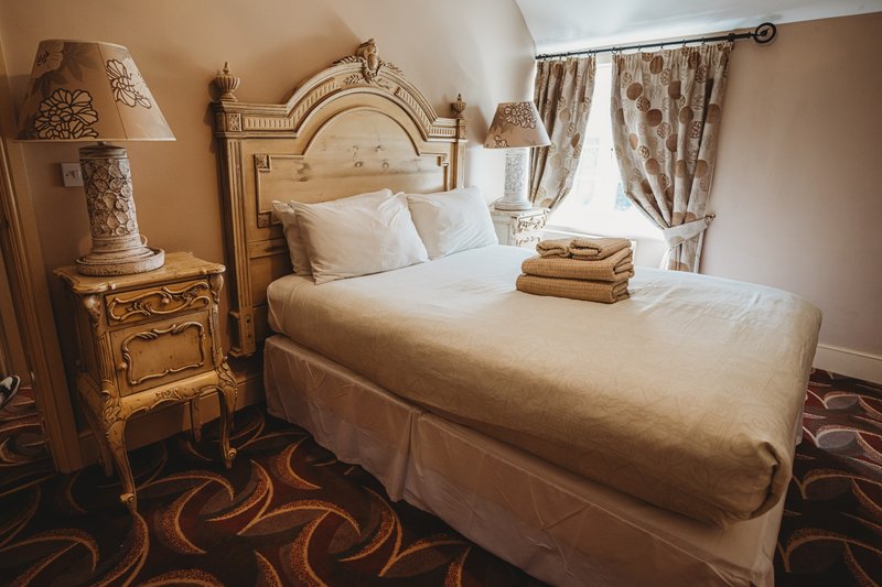 Elegant bedroom with ornate wooden bed, cream linens, bedside lamp, and patterned carpet