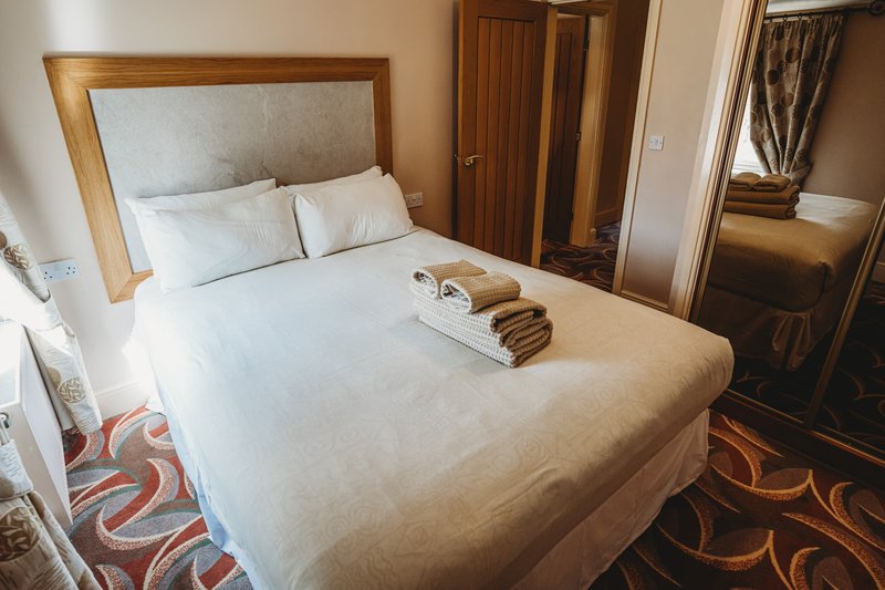 Bedroom with wooden-framed bed, cream bedding, folded towels, wooden doors and patterned carpet.