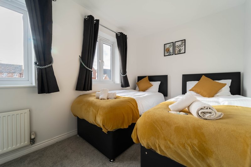 Twin bedroom with black beds, golden bedding, black curtains and city view