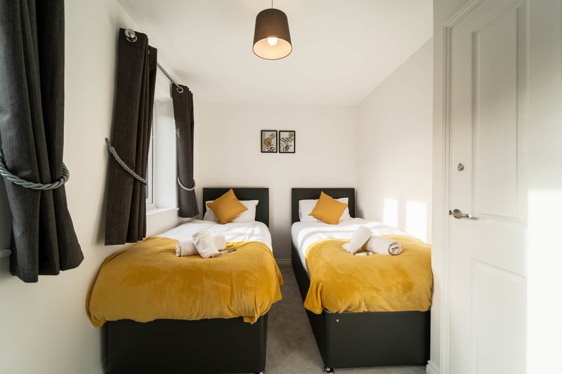Twin bedroom with two single beds, yellow bedding, black headboards, and pendant light