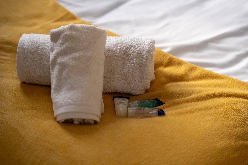 Rolled white towels and toiletries on yellow and white bedding