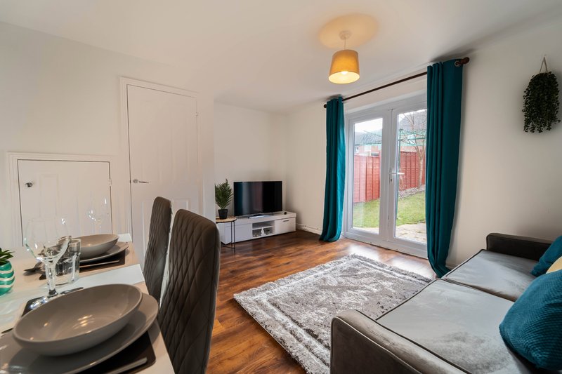Open-plan living area with dining table, sofa, TV stand, and patio doors to garden