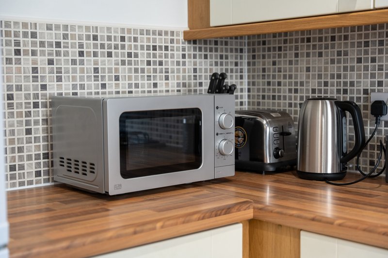 Kitchen counter with microwave, toaster, and electric kettle against tiled backsplash