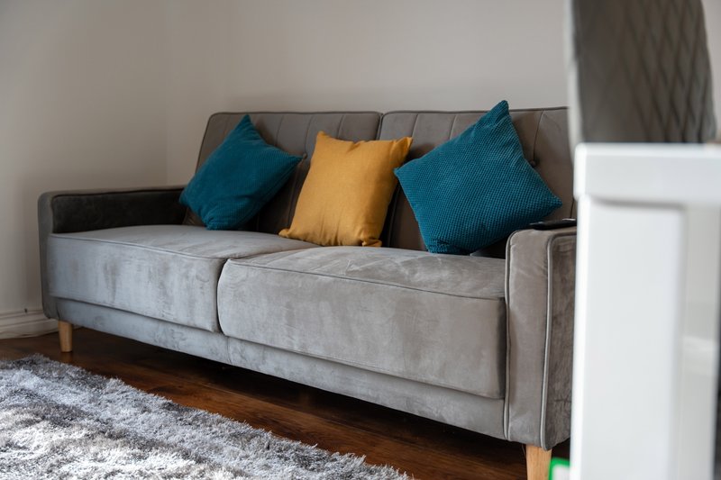 Modern grey upholstered sofa with blue and yellow cushions, wooden floor and area rug