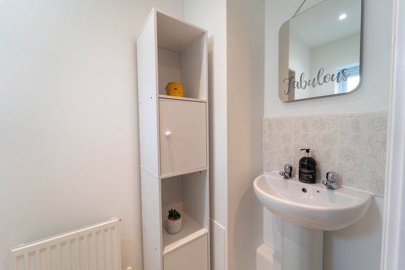 Modern bathroom with pedestal sink, mirror, wall-mounted shelving and radiator
