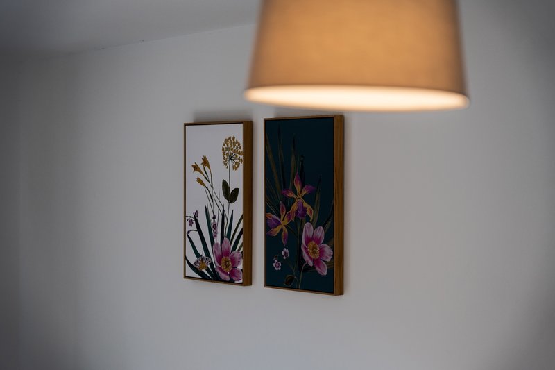 Wall-mounted pendant lamp above two framed botanical artwork prints with flowers